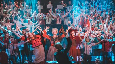 Choir dressed in Christmas attire raising their arms and singing