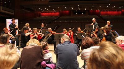 An orchestra on stage with parents and children sat on the floor watching them perform