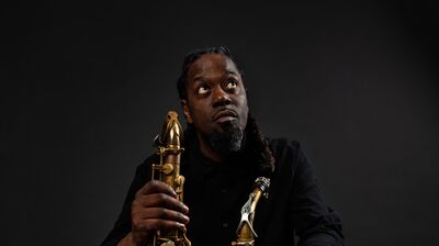 A person wearing all black and red trainers looking up and holding two saxophones