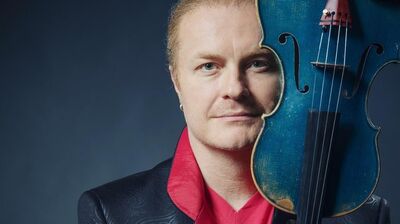 Artist slightly smiling, wearing a red shirt, proudly holding up his deep blue violin