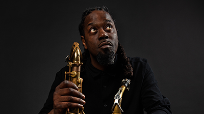 A person wearing all black and red trainers looking up and holding two saxophones