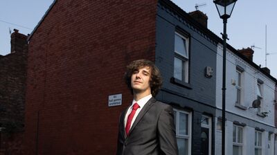 A man wearing a suit with a red tie, and is standing in a street