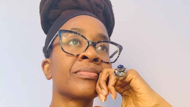 Author Nnedi Okorafor wearing a black T shirt resting her head on her hand.