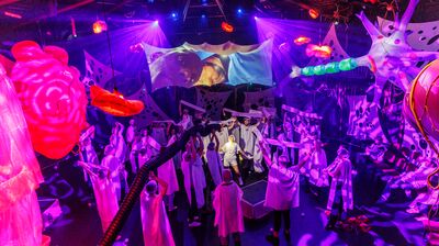 A group of performers on stage, holding white banners in the air with floating inflatable organs hanging from the ceiling