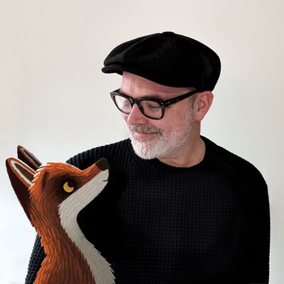 Rob Biddulph wearing a black shirt, hat and glasses, looking at an illustration of a fox.