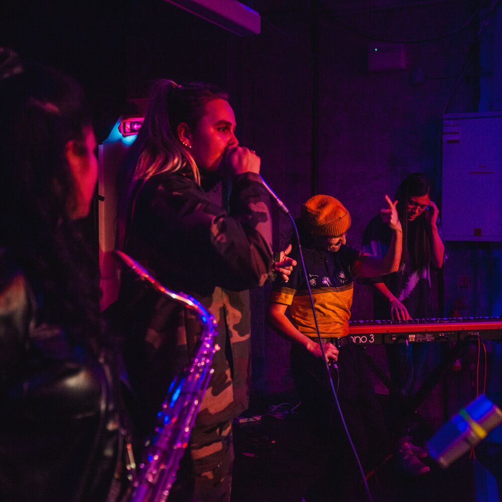 Four musicians on stage either playing an instrument or singing into a microphone