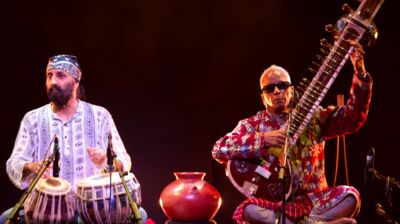 Two performers sat cross-legged on stage one playing tabla and another playing a sitar