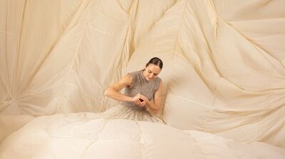 An artist knelt down in a dress that billows out to cover the whole environment, holding something delicately between hands.