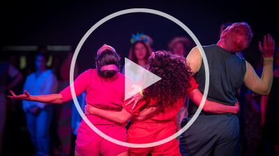 Three performers dance together, with their arms around each other's waists, drenched in pink light.