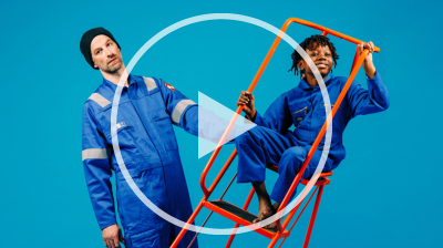 Two performers dressed in blue boiler suits stand in space together; a man holding an orange ladder which a small boy is sat in.