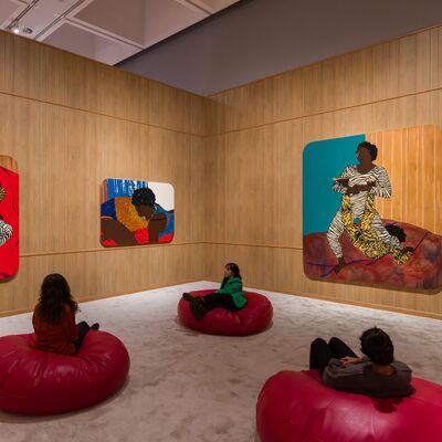 Three people relaxing on red bean bags, staring at large collages on a wood panelled walls
