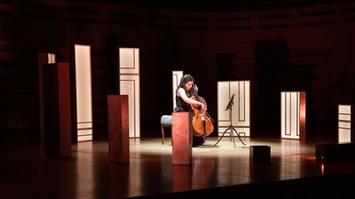 A cellist on stage, surrounded by rectangular box lighting