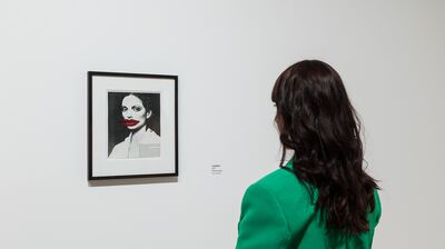 Someone looking at a black and white image framed on a wall, with large red lips collaged on top