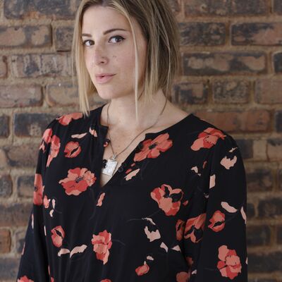 Torrey Peters wearing a flowery top standing against a brick wall.