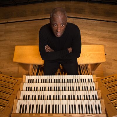 An organist sat behind an organ with their arms crossed looking up at the camera
