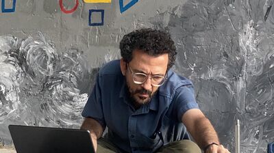 Man wearing denim shirt leans over to adjust dial in front of laptop and sound system
