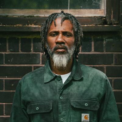 A man with a grey and white beard, wearing a green shirt looking to camera