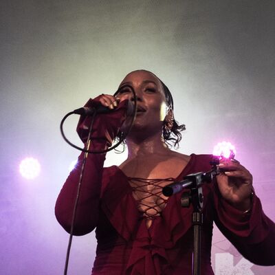 A young woman sings to the crowd in front of purple lights
