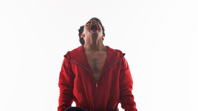 A man wearing a red tracksuit, and holding an electric guitar