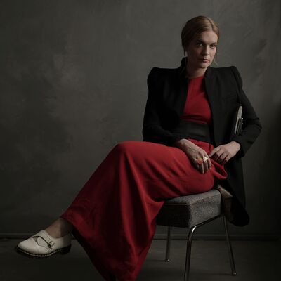 Ruby Hughes is seated wearing a long red dress