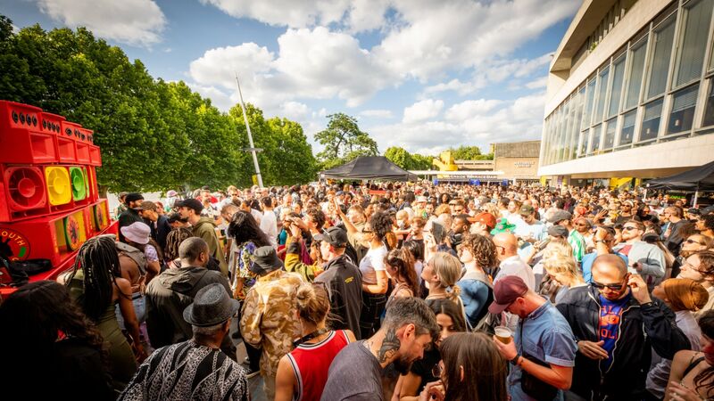 A large crowd of people on the riverside terrace standing in front of a soundsystem