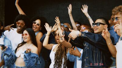 Group of young people wearing blue denim and white t-shirts, all wearing sunglasses lifting their arms up