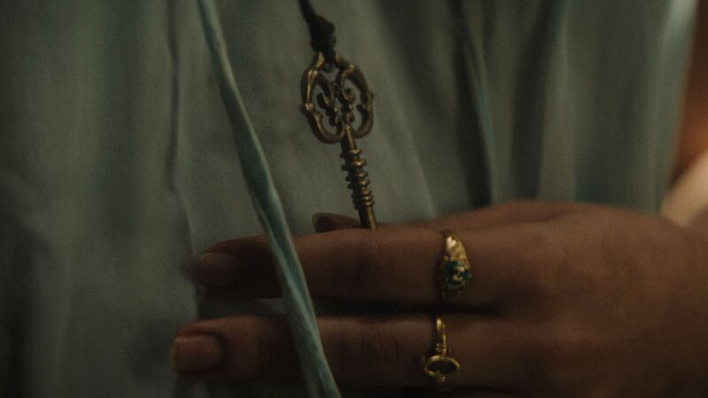 A close-up shot of a woman's hand adorned with delicate gold rings, holding an ornate brass key