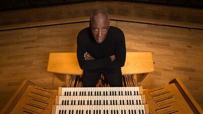 An organist sat behind an organ with their arms crossed looking up at the camera