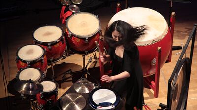 Woman caught in action playing drums, she is wearing all black