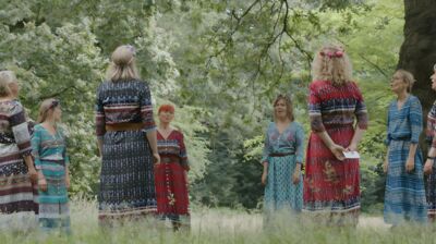 Women stand in a circle in a wood all singing.