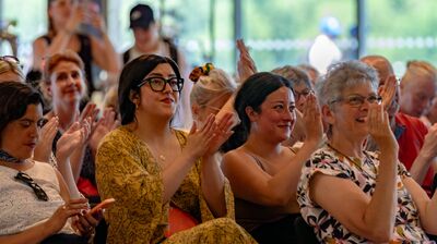 An audience at a Refugee Week event sit clapping.