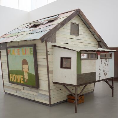 House sculpture inside a white gallery space with the words 'place like home' with a small figure painted on the side