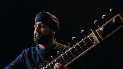 man with turban looking out dressed in dark blue and playing an instrument