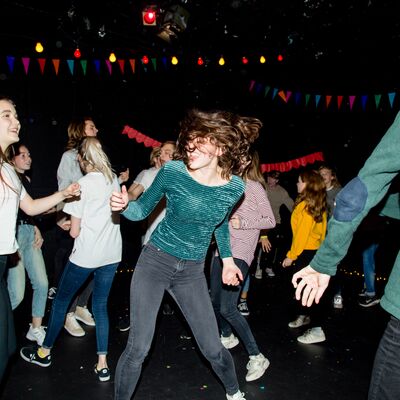 Group of young people dancing in a dark room with bunting and fairy lights, they are smiling and talking