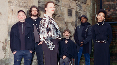 A group of musicians stood against a brick wall