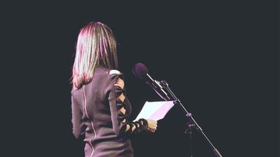 Woman in a maroon top stands at a microphone.