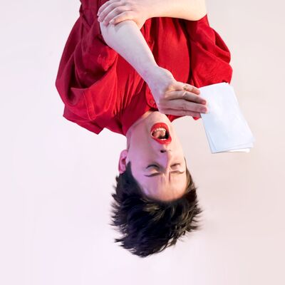 An upside down person with their hanging off their head reads off a small piece of white paper.