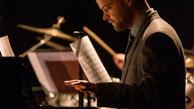 A dark photograph of a pianist deep in concentration, his hand suspended in mid-air before he begins playing