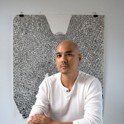 A person wearing white, looking to the camera with a silver artwork behind them and a drawing in front