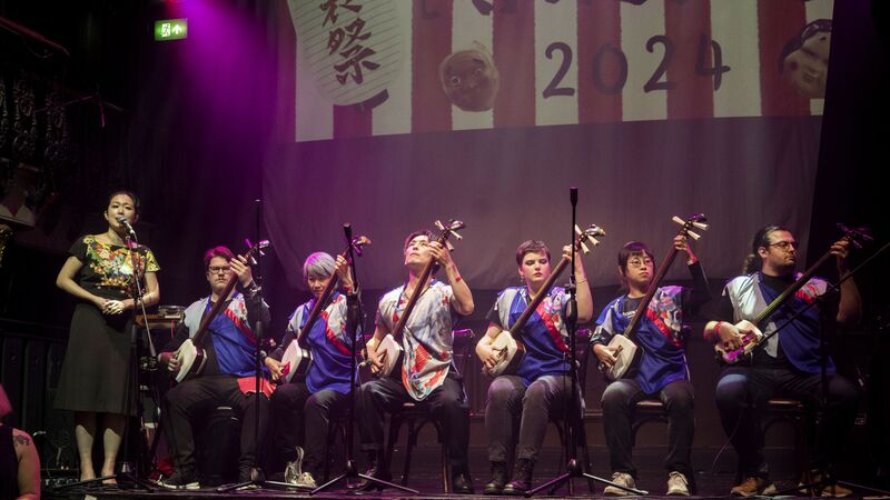 A group of performers on stage playing instruments and one woman singing.