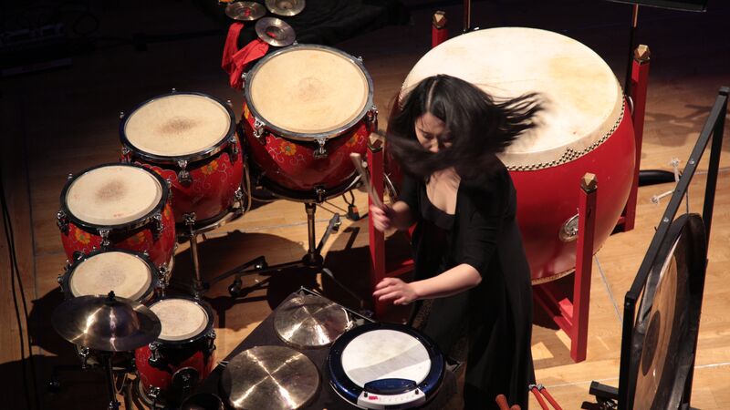 Woman caught in action playing drums, she is wearing all black