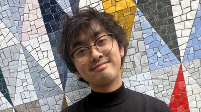 Person wearing black turtle neck standing in front of colourful mosaic wall