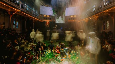 Group of people all wearing white hoodies moving in a blur through a large space with audience