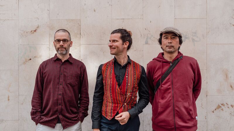 Three mean wearing red shirts, standing against a pale marble wall