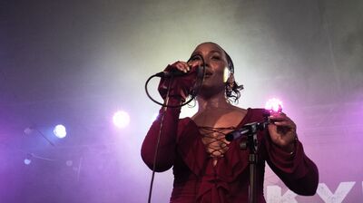 A young woman sings to the crowd in front of purple lights