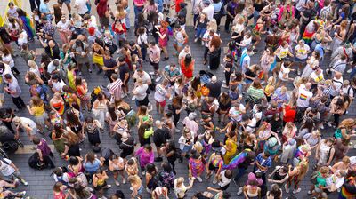 A Birdseye view of people having fun with pride flags on their clothes outside on the roof terrace.