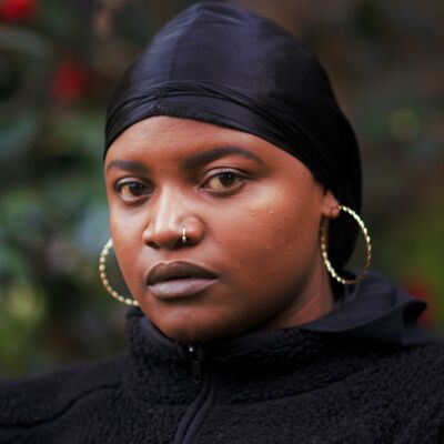 A person wearing black and large gold hoop earrings and a nose ring. They have deep brown eyes