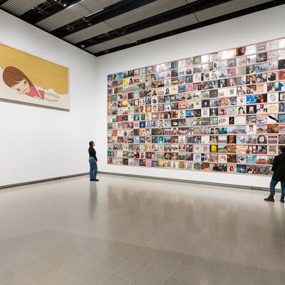 Two people in a large exhibition space looking at a collection of records displayed on one wall