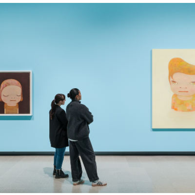 Two people in an exhibiton space with blue painted walls and two artworks of figures hanging on the wall