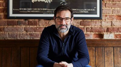 Adam Buxton, comedian sits at a pub against a brick background.